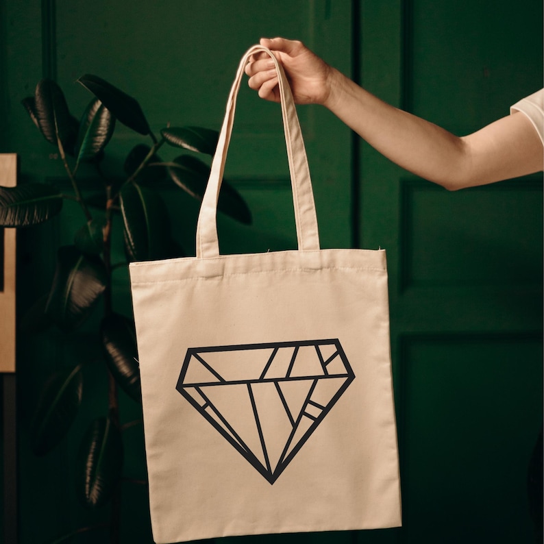 May include: A beige tote bag with a black diamond design. The diamond is made up of many small lines.