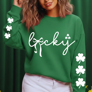 May include: Green sweatshirt with the word "Lucky" in white script. The sweatshirt has white shamrock designs on the sleeves and near the word "Lucky". The sweatshirt is a St. Patrick's Day themed apparel item.