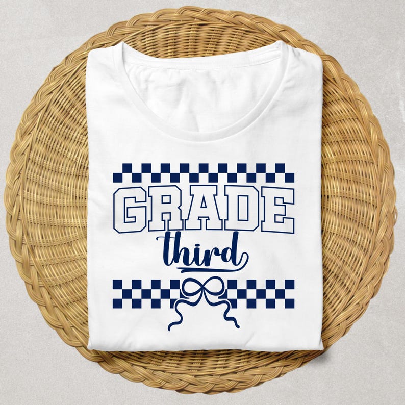 Op de afbeelding: Wit T-shirt met de tekst "GRADE third" in marineblauw. Het woord "GRADE" is in een vetgedrukte, blokletter, en "third" is cursief. Het ontwerp bevat marineblauwe geblokte patronen boven en onder de tekst, en een strik-afbeelding.