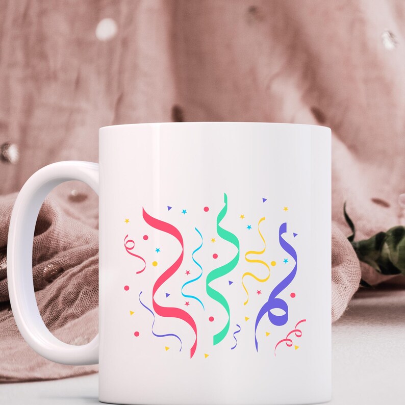 K&ouml;nnte beinhalten: Wei&szlig;e Keramiktasse mit einem bunten Konfetti-Design. Das Design zeigt rote, blaue, gr&uuml;ne und gelbe Konfetti-Serpentinen mit Sternen und Punkten.