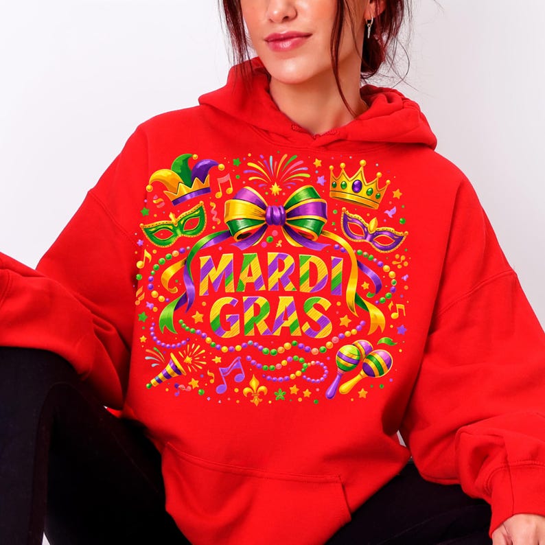 May include: A red hoodie featuring a colorful Mardi Gras design. The graphic includes a bow, crown, masks, musical notes, and the words "MARDI GRAS" in a vibrant, multi-colored font. The design is festive and eye-catching.