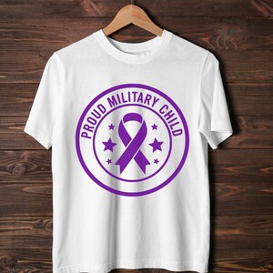 May include: White t-shirt with a purple circular design. The design features the text "PROUD MILITARY CHILD" around a purple ribbon and stars. The shirt is hanging on a wooden hanger.