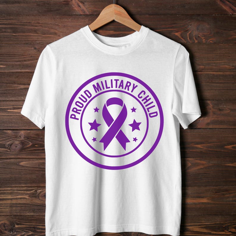 May include: White t-shirt with a purple circular design. The design features the text "PROUD MILITARY CHILD" around a purple ribbon and stars. The shirt is hanging on a wooden hanger.