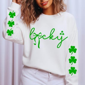 May include: White sweatshirt with the word "Lucky" in green script. The letter "y" is adorned with three green shamrocks. Green shamrocks are also on the sleeves. A St. Patrick's Day themed apparel item.