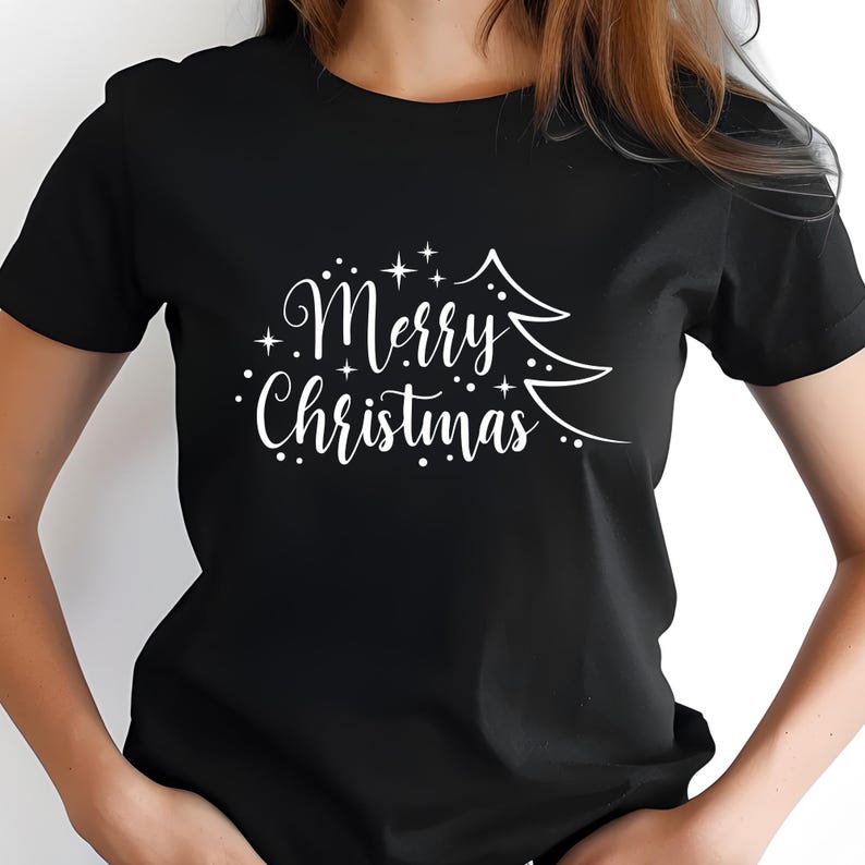 May include: Black t-shirt with the words "Merry Christmas" in a decorative script, accompanied by a stylized Christmas tree graphic. The white text and tree design contrast sharply against the dark background, creating a festive holiday theme.
