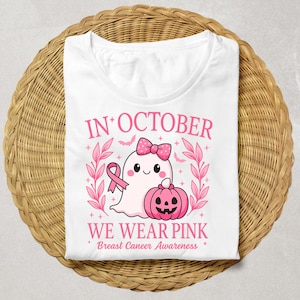 May include: White t-shirt with a pink graphic design. The design includes a cute ghost wearing a bow, a pink ribbon, and a jack-o'-lantern. The text reads "IN OCTOBER WE WEAR PINK Breast Cancer Awareness."