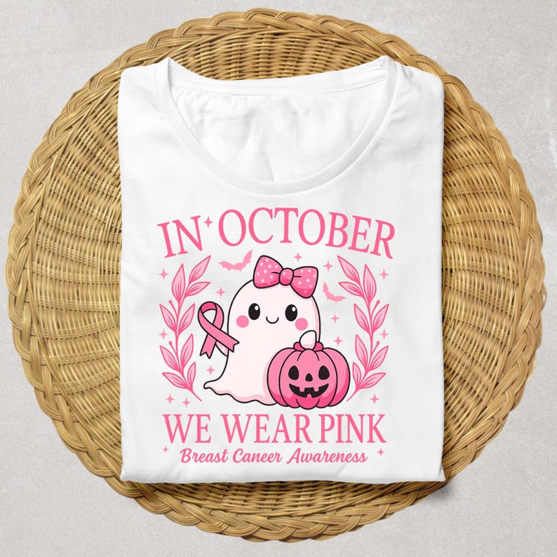 May include: White t-shirt with a pink graphic design. The design includes a cute ghost wearing a bow, a pink ribbon, and a jack-o'-lantern. The text reads "IN OCTOBER WE WEAR PINK Breast Cancer Awareness."