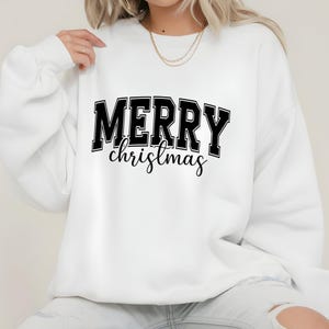 May include: White sweatshirt with the text "MERRY christmas" in black block letters and cursive script. The sweatshirt is a crew neck style, perfect for the holiday season. The design is centered on the front of the garment.