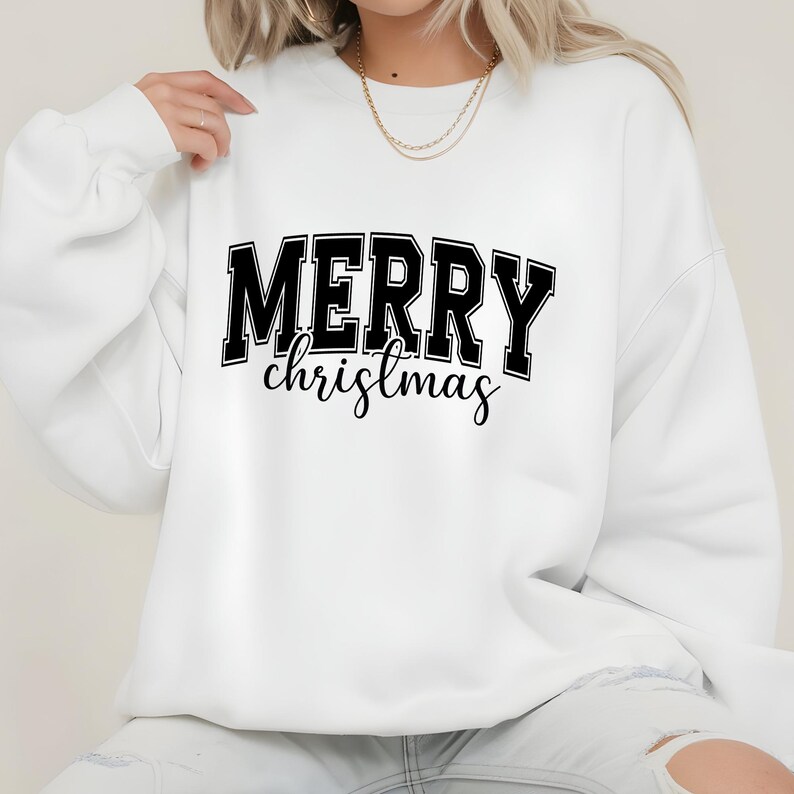 May include: White sweatshirt with the text "MERRY christmas" in black block letters and cursive script. The sweatshirt is a crew neck style, perfect for the holiday season. The design is centered on the front of the garment.