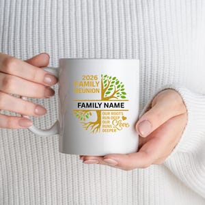 Op de afbeelding: Witte keramische mok met een gouden en groen boomontwerp, met de tekst "2026 Family Reunion" en ruimte voor een familienaam. De mok bevat ook de zin "Onze wortels gaan diep, onze liefde gaat dieper."