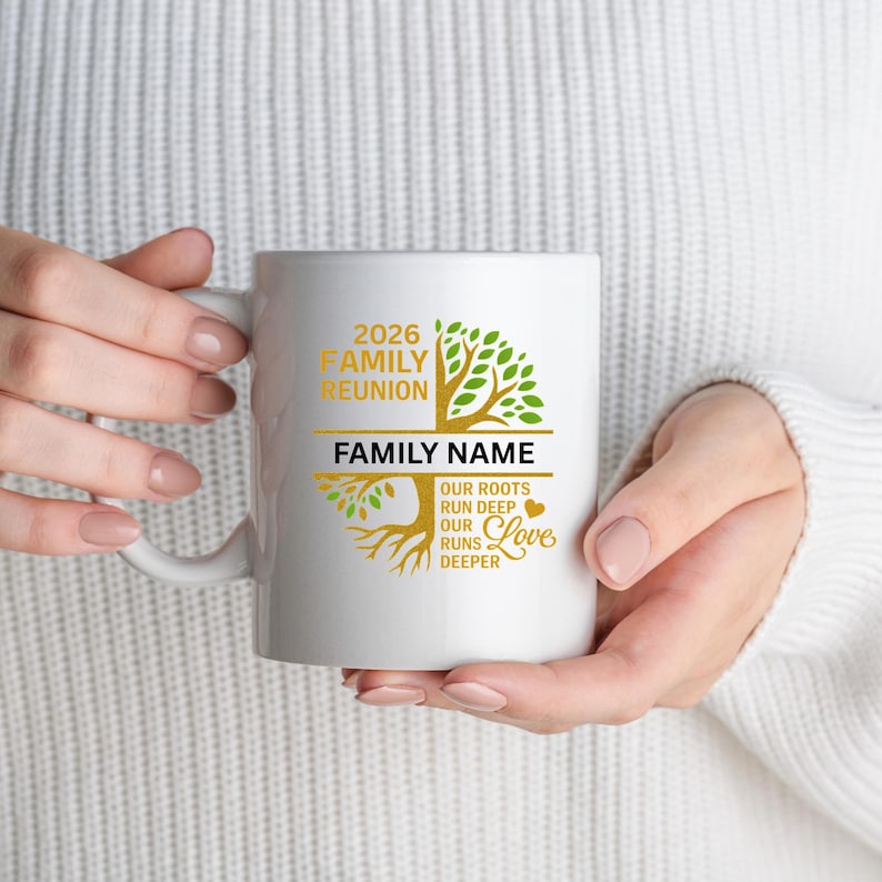 Op de afbeelding: Witte keramische mok met een gouden en groen boomontwerp, met de tekst "2026 Family Reunion" en ruimte voor een familienaam. De mok bevat ook de zin "Onze wortels gaan diep, onze liefde gaat dieper."