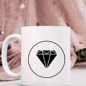 May include: White ceramic mug with a black diamond graphic inside a circle. The diamond is a geometric shape with multiple points.