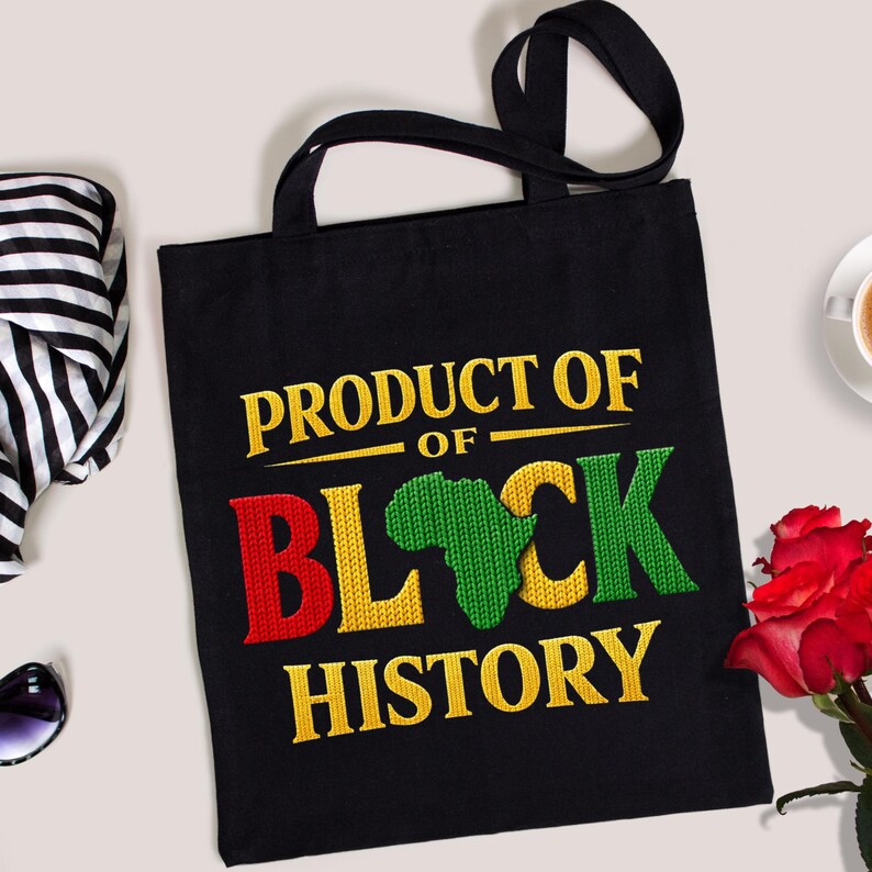 K&ouml;nnte beinhalten: Schwarze Tragetasche mit dem Text "PRODUCT OF BLACK HISTORY" in Gelb, Rot und Gr&uuml;n. Das Design beinhaltet eine Umrisszeichnung des afrikanischen Kontinents. Die Tasche hat schwarze Griffe.