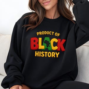 K&ouml;nnte beinhalten: Schwarzes Sweatshirt mit dem Text "PRODUCT OF BLACK HISTORY" in Gelb, Rot, Gr&uuml;n und Schwarz. Das Wort "BLACK" zeigt eine Karte von Afrika. Das Sweatshirt hat einen Rundhalsausschnitt.