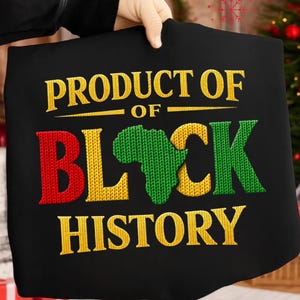 K&ouml;nnte beinhalten: Schwarzes T-Shirt mit dem Text "PRODUCT OF BLACK HISTORY" in Gelb, Rot und Gr&uuml;n. Das Wort "BLACK" zeigt ein gr&uuml;nes Afrika-Karten-Design. Der Text ist auf das Shirt gestickt.