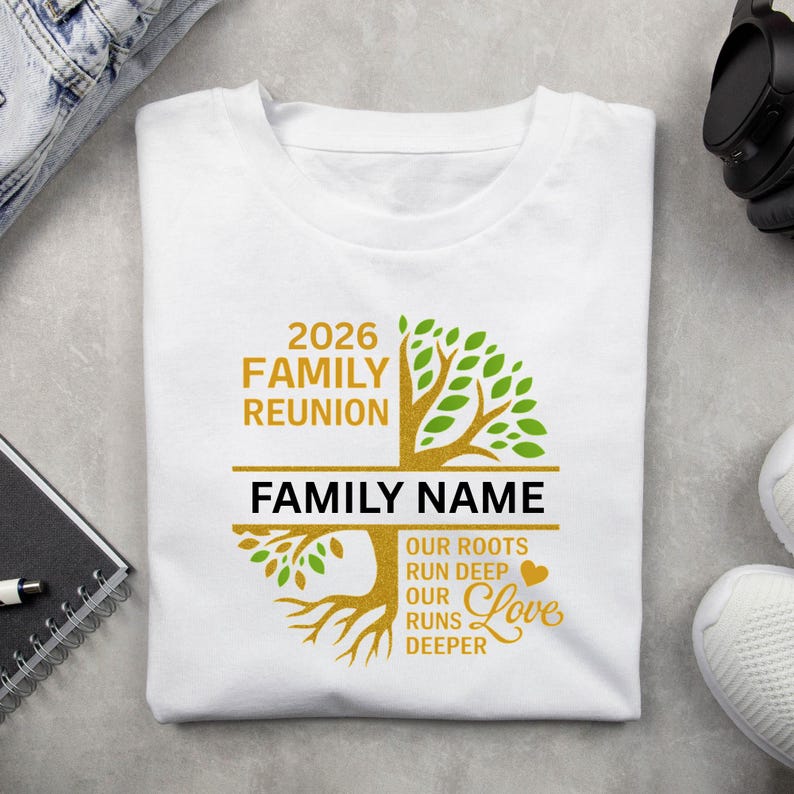 Op de afbeelding: Wit t-shirt met een familiere&uuml;nie-ontwerp. Het ontwerp bevat de tekst "2026 Family Reunion" en "Family Name" boven en onder een boomafbeelding. De boom heeft groene bladeren en een gouden stam en wortels. De tekst "Our roots run deep, our love runs deeper" is ook opgenomen.