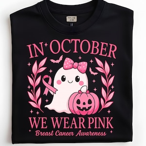 May include: Black t-shirt with a pink graphic. The graphic includes the text "IN OCTOBER WE WEAR PINK Breast Cancer Awareness" with a ghost, pumpkin, and pink ribbon design.