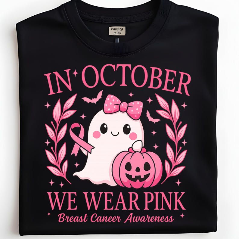 May include: Black t-shirt with a pink graphic. The graphic includes the text "IN OCTOBER WE WEAR PINK Breast Cancer Awareness" with a ghost, pumpkin, and pink ribbon design.