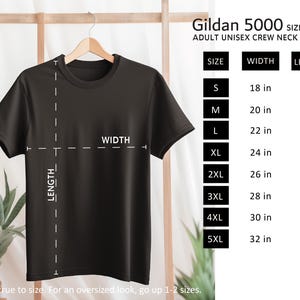 May include: A black Gildan 5000 adult unisex crew neck t-shirt hanging on a wooden hanger. The image includes a size guide with measurements in inches for sizes S to 5XL. The text says, "Fits true to size. For an oversized look, go up 1-2 sizes."