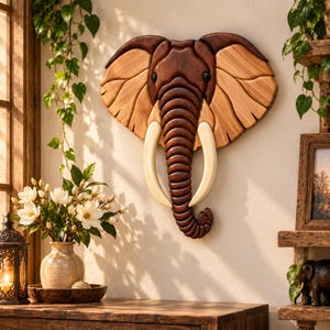May include: A wall-mounted elephant head sculpture crafted from wood, featuring a dark brown trunk and forehead, lighter tan ears with carved grain details, and two smooth, cream-colored tusks extending downward from the face.