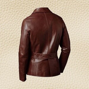 May include: A brown leather jacket with a notched collar and a belt at the waist. The jacket has long sleeves and a tailored fit. The leather appears to have a slight sheen, and the overall style is classic and sophisticated.