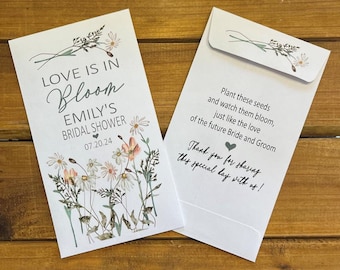 May include: White envelope with a floral design and the text "LOVE IS IN BLOOM EMILY'S BRIDAL SHOWER 07.20.24". The back of the envelope has the text "Plant these seeds and watch them bloom, just like the love of the future Bride and Groom. Thank you for sharing this special day with us!"