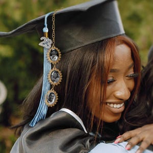 May include: A blue and gold graduation tassel with a charm featuring three framed photos. The tassel is attached to a graduation cap.
