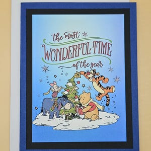 May include: A Christmas greeting card featuring Winnie the Pooh and friends. The card has a blue background with the text "the most WONDERFUL TIME of the year". The characters are gathered around a decorated Christmas tree.