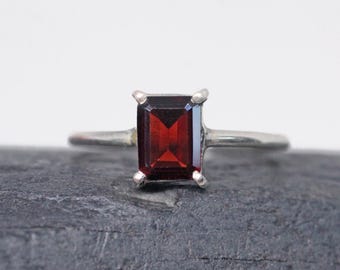 Könnte beinhalten: Ein silberner Ring mit einem roten Edelstein in quadratischer Form.