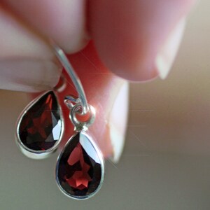 Puede incluir: Un par de pendientes de plata con piedras de granate rojo en forma de l&aacute;grima.