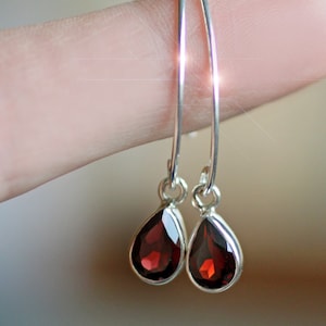 Puede incluir: Un par de pendientes de aro de plata con piedras de granate rojo en forma de l&aacute;grima.