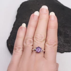 May include: A silver ring with a purple gemstone set in a hexagonal shape.