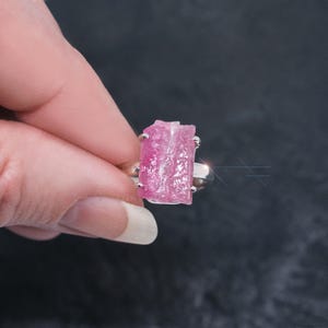 May include: A silver ring with a pink, raw, rectangular gemstone. The gemstone has a natural, rough texture.