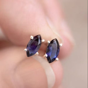 Peut inclure: Une paire de boucles d'oreilles à clous avec des pierres précieuses bleu foncé taillées en marquise, serties dans des griffes en métal argenté. Chaque boucle présente une forme ovale pointue aux facettes réfléchissantes et éclatantes.