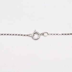 May include: Close-up of a silver necklace chain with a circular clasp. The chain is made of small, rectangular links. The clasp is a spring ring type, commonly used for jewelry. The background is plain white.