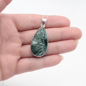 May include: A teardrop-shaped pendant with a silver-colored bezel and chain. The pendant features a green and white stone with a unique, textured pattern. The necklace is displayed against a neutral background.