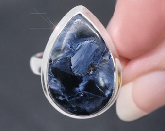 May include: A silver ring with a teardrop-shaped blue tiger's eye gemstone. The ring is set in a silver band and the gemstone has a unique pattern of blue and gold.