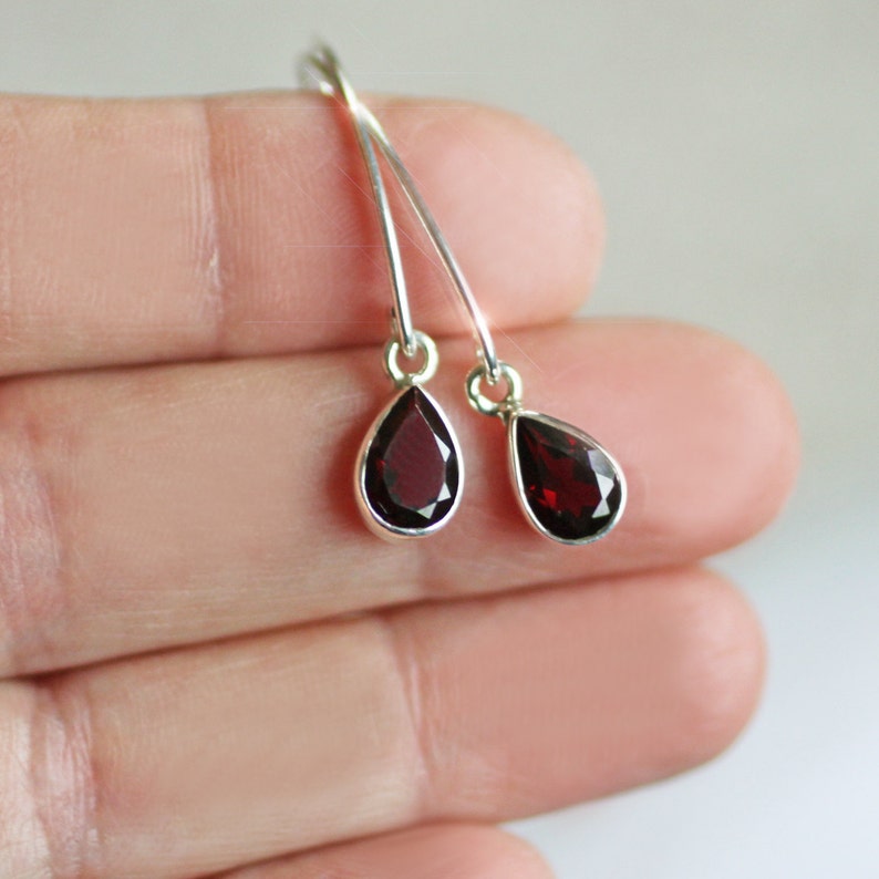 Puede incluir: Un par de pendientes de plata con piedras de granate rojo en forma de l&aacute;grima.