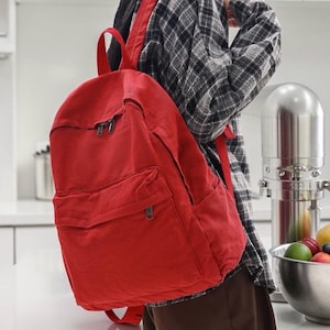 May include: A red backpack with a front pocket and two zipped compartments. The backpack has adjustable shoulder straps and a top handle. The bag is made of a durable fabric and is suitable for carrying books, supplies, or personal items.