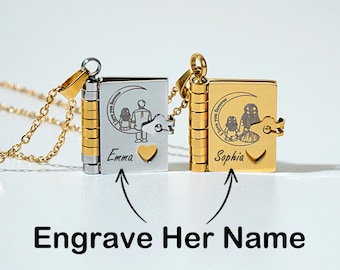 Puede incluir: Dos collares colgantes personalizados con forma de libro. Uno es plateado, el otro dorado. Cada uno presenta una silueta familiar bajo una luna creciente, con los nombres "Emma" y "Sophia" grabados. También se ve el texto "Engrave Her Name".