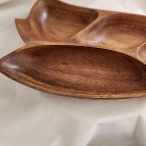 May include: A wooden serving tray with a leaf-like design. The tray is divided into four sections, perfect for serving snacks or appetizers. The wood has a warm, brown tone, and the tray has a smooth, polished finish.