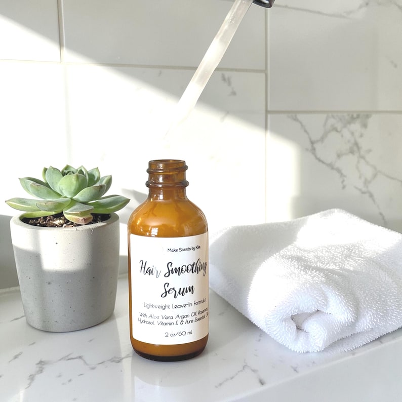 May include: An amber glass bottle of Hair Smoothing Serum with a white label featuring black text that reads Make Scents by Kim, Hair Smoothing Serum, Lightweight Leave-in Formula, With Aloe Vera, Argan Oil, Rosemary Hydrosol, Vitamin E & Pure Essential Oils, 2 oz/60 ml.