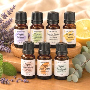 May include: Seven amber glass bottles of Make Scents by Kim essential oils, each 10 ml, labeled Organic Lavender, Peppermint, Rosemary, Lemon, Frankincense Serrata, Sweet Orange, and Eucalyptus, arranged on a round wooden base with botanical accents.
