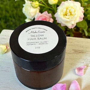 May include: A brown jar of Tallow Hair Balm with a black lid, labeled "Make Scents." The label lists ingredients: organic beef tallow, jojoba oil, and argan oil. The jar is 2 oz. The background features pink and white roses.