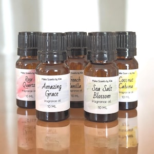 May include: Six small brown glass bottles with black lids, each containing 10 ml of fragrance oil. The bottles are labeled with different scents: Rose Quartz, Amazing Grace, French Vanilla, Sea Salt Blossom, Coconut Cabana.