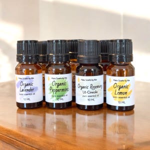 May include: A collection of small amber glass bottles with black caps, each labeled with the name of an organic essential oil. The labels include "Organic Lavender," "Organic Peppermint," "Organic Rosemary," and "Organic Lemon." Each bottle contains 10 mL of oil.