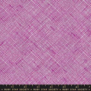 May include: A magenta fabric with a white cross-hatched grid pattern. A black ruler at the bottom shows measurements up to 7 inches. The fabric is labeled with the text Ruby Star Society repeated along the bottom edge of the material.