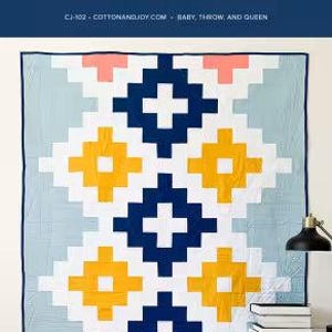 May include: A geometric quilt with a blue, white, yellow, and pink pattern. The quilt is labeled "Andes Ode" and "Cotton + Joy". The design features a repeating cross motif. The quilt is displayed on a wall.