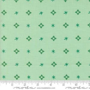 May include: Light green fabric with a repeating pattern of dark green starburst and asterisk shapes. The fabric has a subtle texture and a ruler along the bottom edge with the word "moda" printed on it.