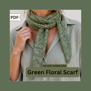May include: A green floral scarf with a white floral pattern is draped around a person's neck. The scarf is made of a soft fabric and is a light green color. The text "Green Floral Scarf" is displayed on the image.